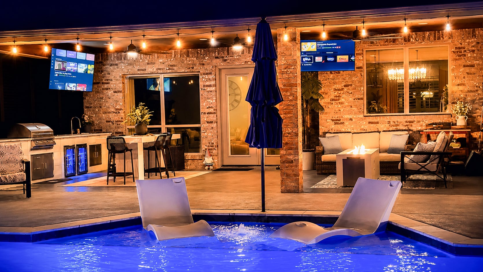 Night view across the illuminated pool toward the covered patio and outdoor kitchen